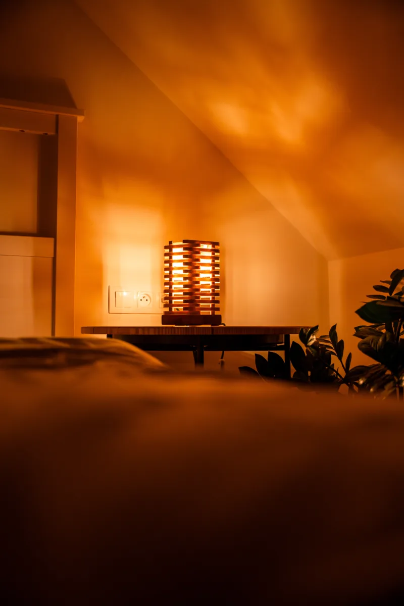 Stolni dřevěná lampa Tria Costa v interiéru potmě se stíny.