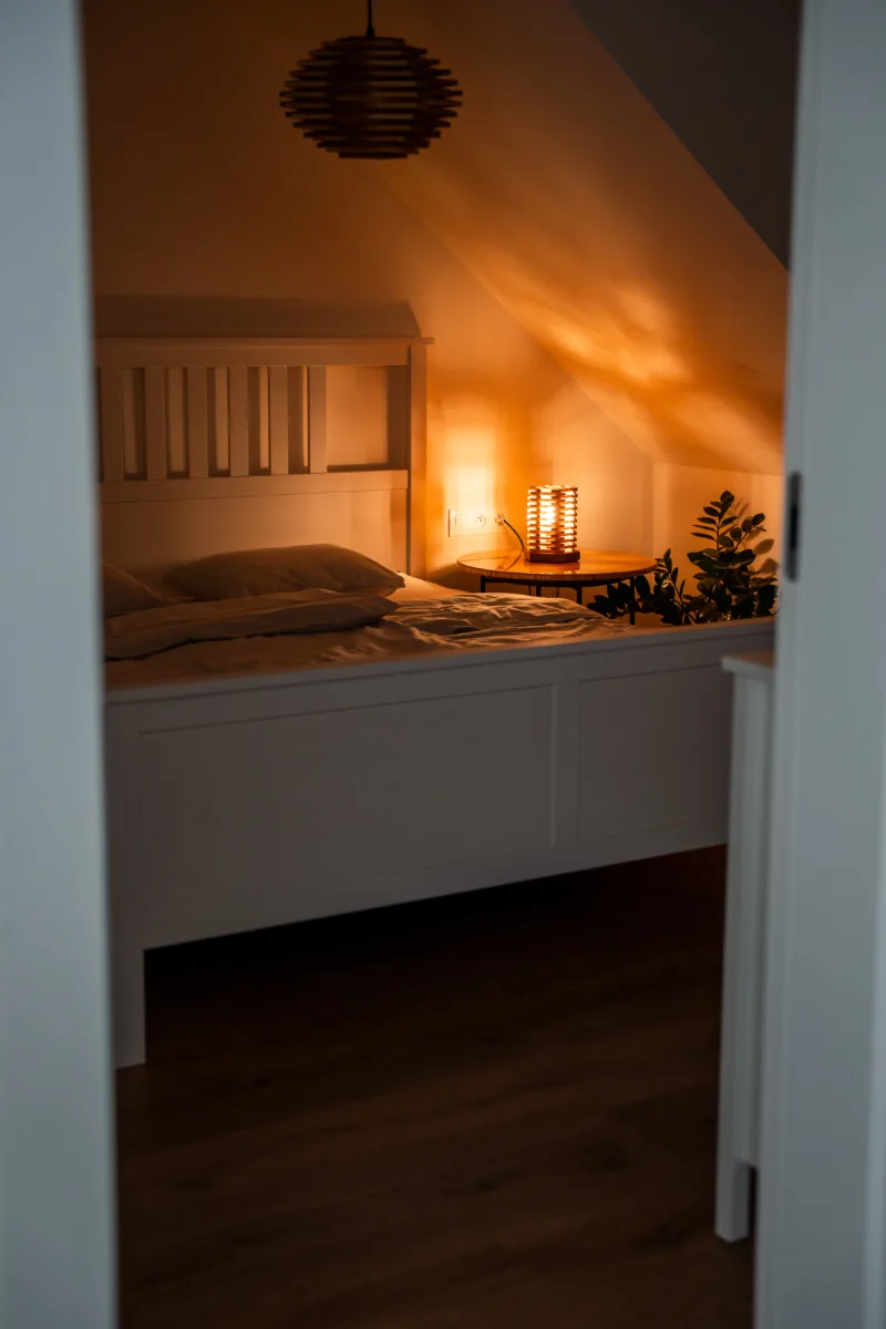 Stolni dřevěná lampa Tria Costa v interiéru potmě zdalky.