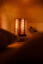 Stolni dřevěná lampa Tria Costa v interiéru potmě zblizka.