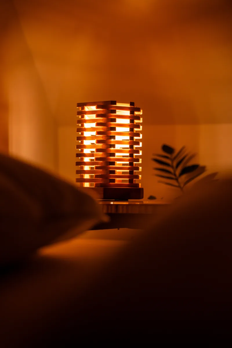 Stolni dřevěná lampa Tria Costa v interiéru potmě zblizka.