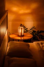 Stolni dřevěná lampa Tria Costa v interiéru potmě ze strany.