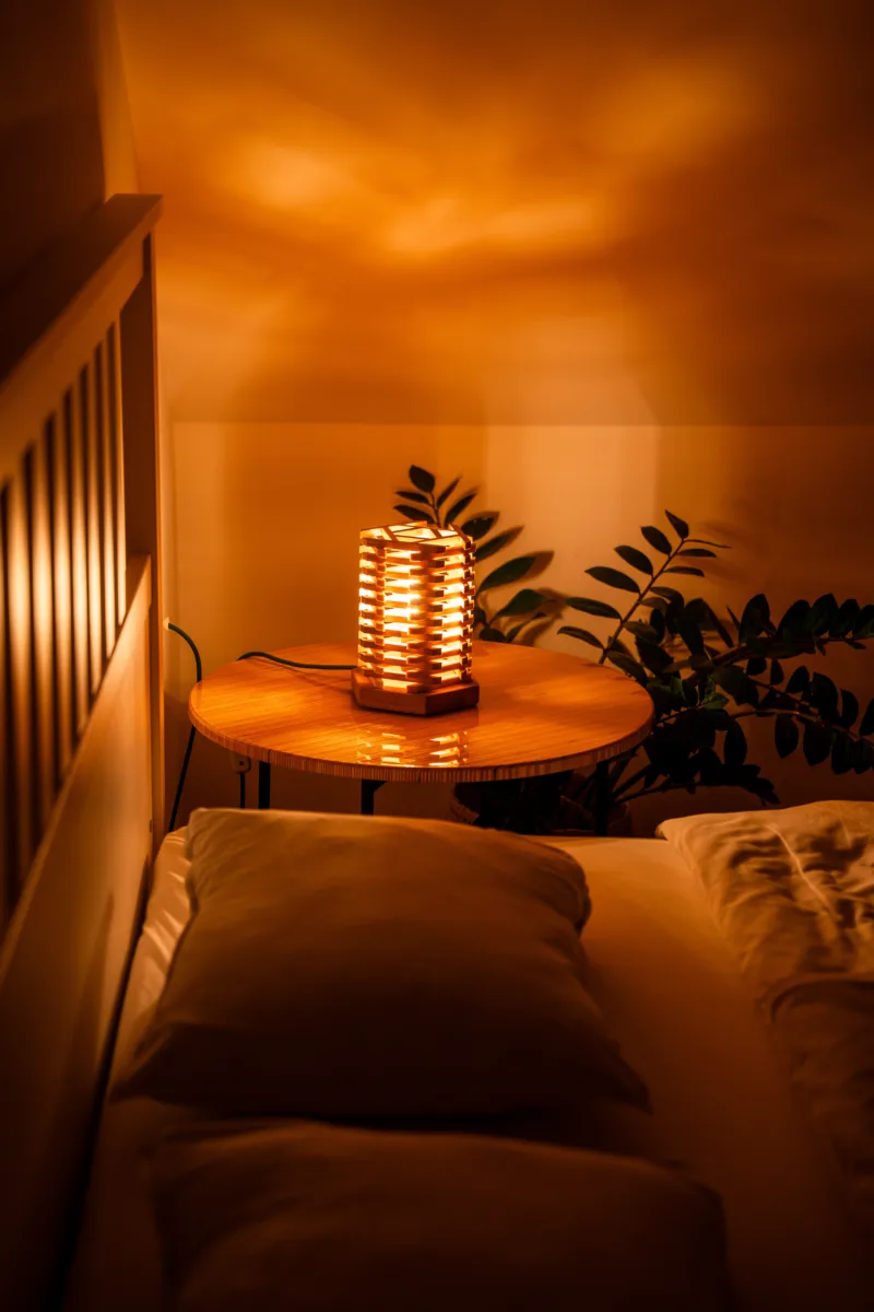 Stolni dřevěná lampa Tria Costa v interiéru potmě ze strany.