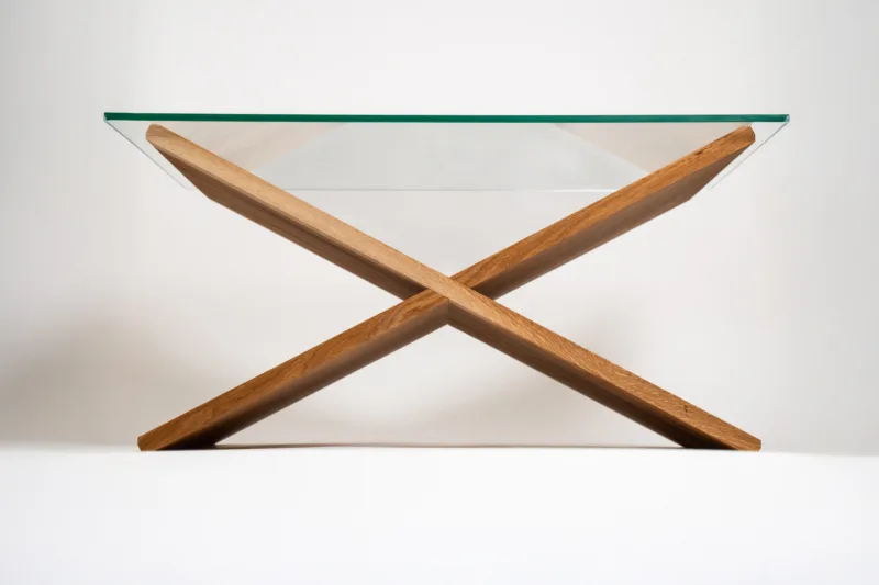 Designový konferenční stůl Bon Feris vyniká minimalistickým X-tvarem podnože z výběrového dubu. Kombinace dřeva s deskou o rozměru 90×55 cm působí vzdušně, ale zároveň stabilně. Pod skleněnou deskou vzniká praktický úložný prostor.