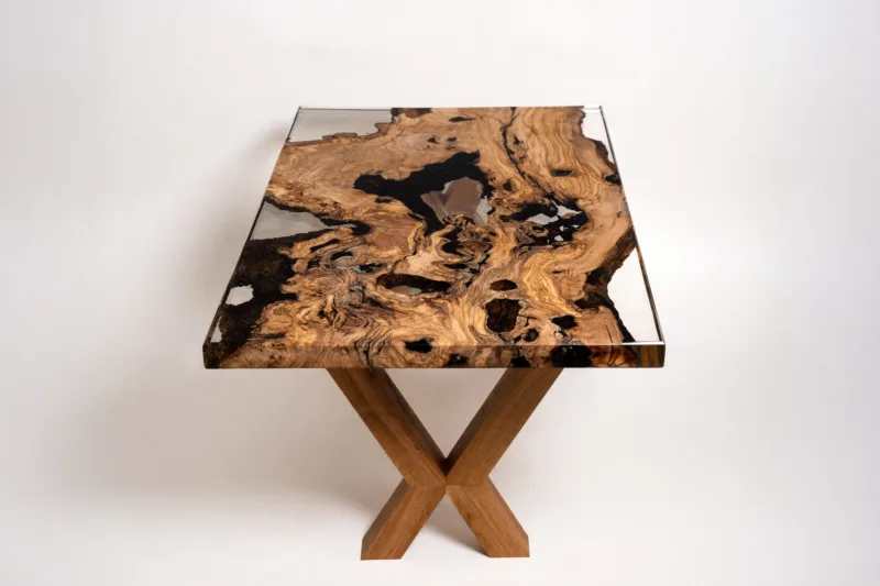 Přirozená struktura olivového dřeva dodává stolové desce Oliv Vetum přírodní vzhled a hluboký charakter. UV stabilní čirá epoxidová pryskyřice s certifikací pro styk s potravinami dodává skleněný dojem, díky kterému nechá kresbu a přirozenost dřeva krásně vyniknout.